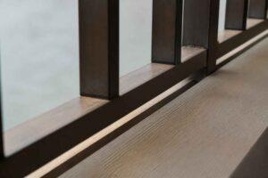 Drewniany parapet i czarne pionowe elementy balustrady przy jasnej ścianie