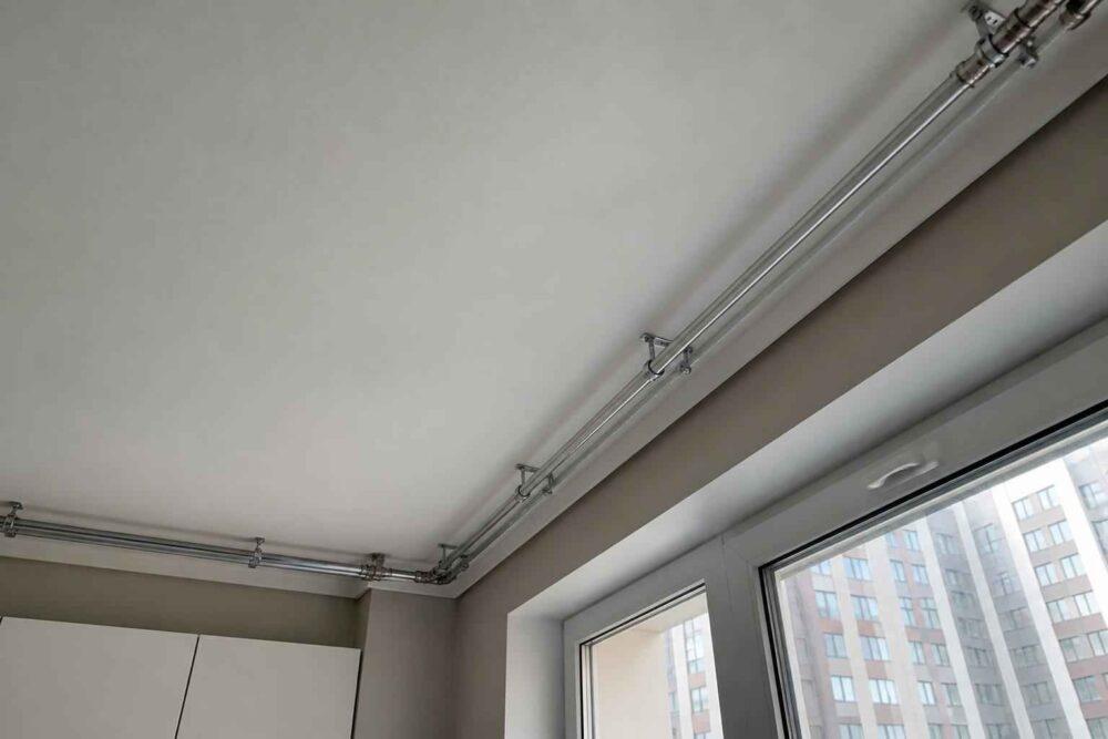 Metalowe przewody instalacji elektrycznej pod sufitem przy dużych oknach mieszkania