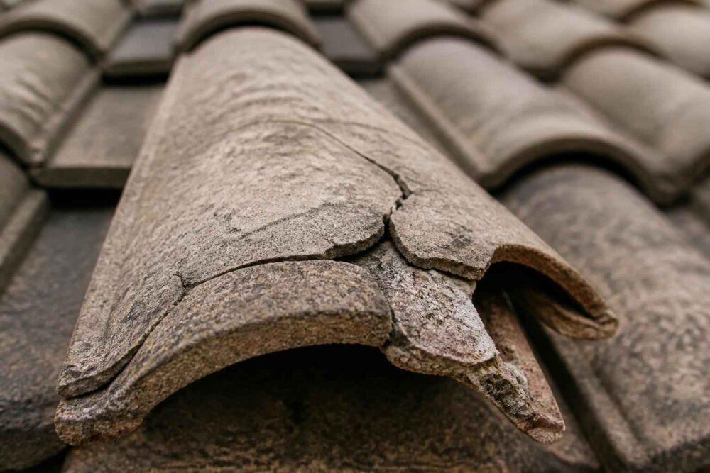 Zniszczona dachówka ceramiczna z widocznymi pęknięciami na tle pokrycia dachowego