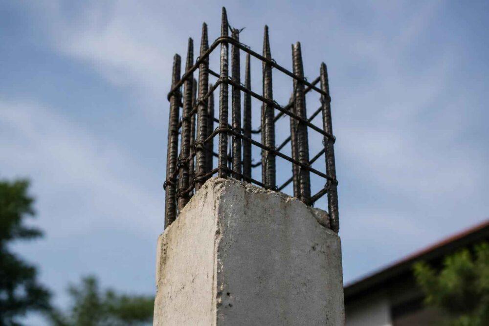 Wystające stalowe pręty zbrojeniowe nad betonowym słupem na tle błękitnego nieba